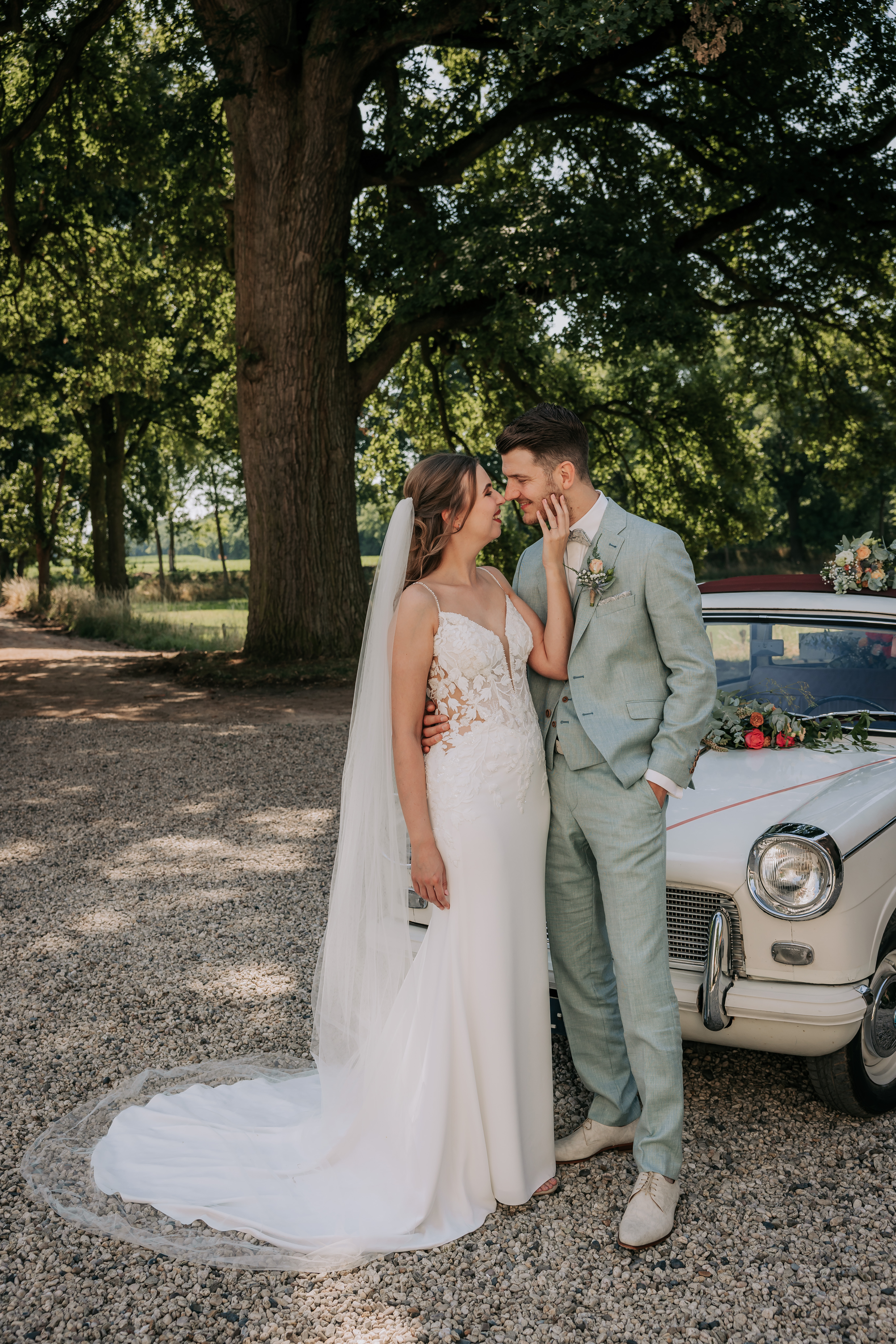 Romantisch bruidspaar, bruid in mermaid trouwjurk met kanten lijfje bij vintage auto op landgoed - Bruidshuis Diana